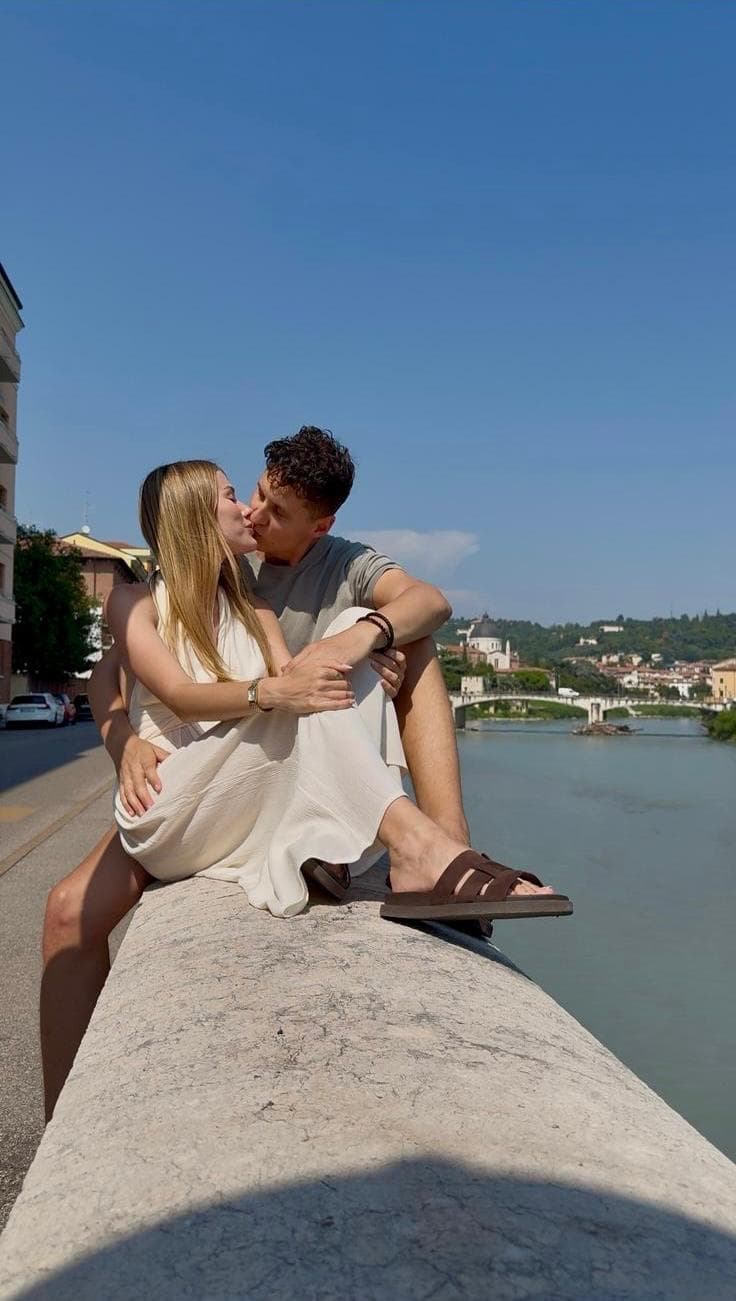 Kateřina Svobodová a Milan Talíř na kamenné zídce nad řekou, v dálce most